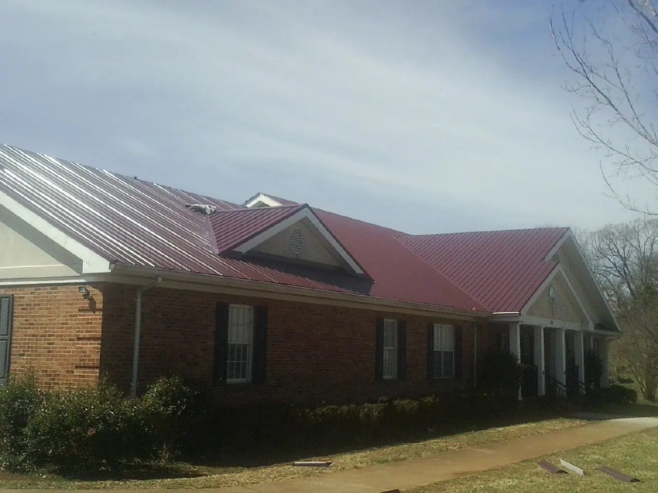 Red metal roof with gabled entries on a long brick building, from a Hail Damage Roof Repair job in Floyd