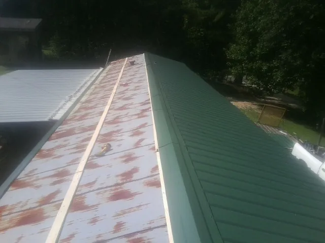 Old rusted panels beside newly installed green metal roofing in Floyd